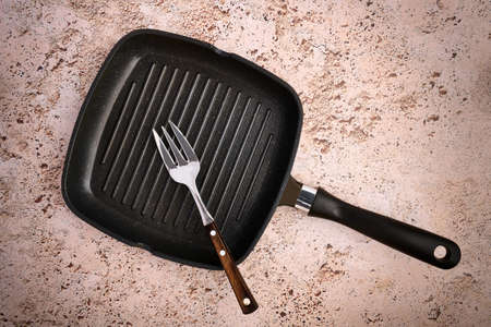 Grill pan and steel meat fork lie on a light concrete background, top viewの写真素材