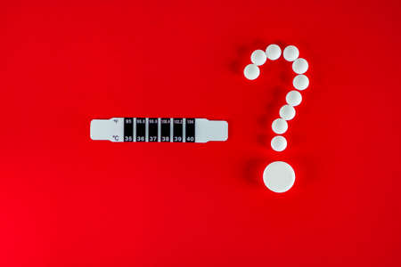 Thermometer and white pills in the form of a question mark on a red background with copy space for text.の写真素材