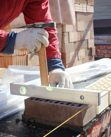 Bricklayers hands with in masonry trowel bricklaying new house wall on foundation. Close up of...