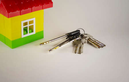 Real estate concept. Small toy house with keys on grey background. With copy space. Selective focus...