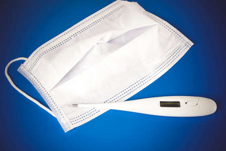 Medical mask and electronic thermometer on yellow background flat lay top view copy space....
