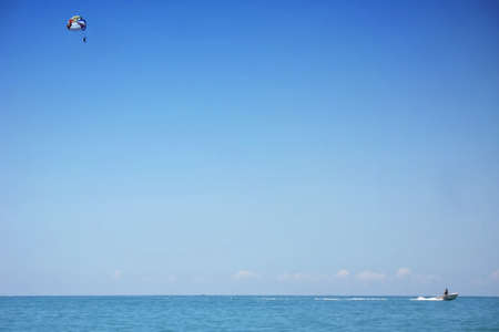 Water attraction - a boat tows a men on a parachute over the sea. Para sailing over sea against blue sky.の写真素材