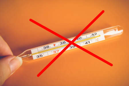 Red cross on a mercury medical thermometer on orange background. Prohibition on the use of mercury thermometers. Protection against virus, coronavirus, flu, colds. Medical tool, concept of healthの写真素材