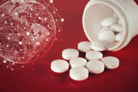 Pills spilling out of pill bottle with virtual hologram earth on a red background. Medicine,...