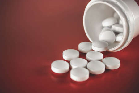 Pills spilling out of pill bottle on a red background. Medicine, pharmacy and healthcare. Empty...