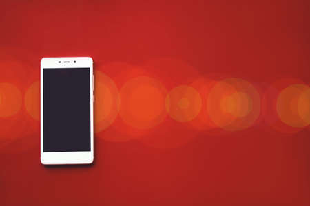 Mockup image of white mobile phone on red background with blank black screen and bokehの写真素材
