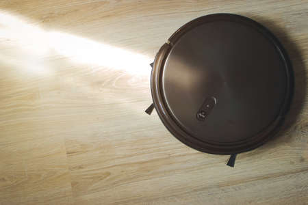 robotic vacuum cleaner on laminate floor in action. housework and technology concept