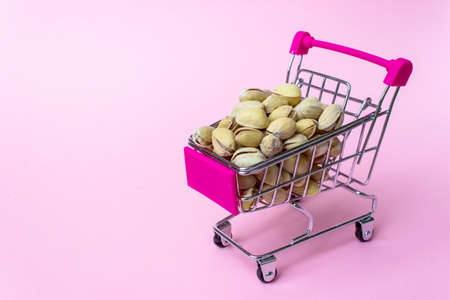 Stainless steel small miniature toy shopping trolley with pistachio nuts inside on pink background....