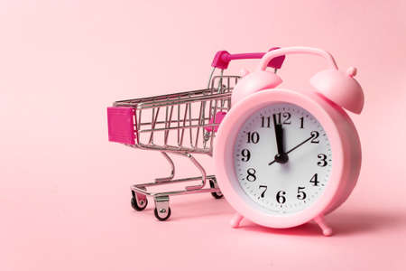 Close-Up Of Alarm Clock and Shopping Cart Against Pink Background. Sale, discount time, time saving...