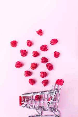 Raspberries falling in shopping cart on pink background. Healthy meals shopping, cornucopia and...