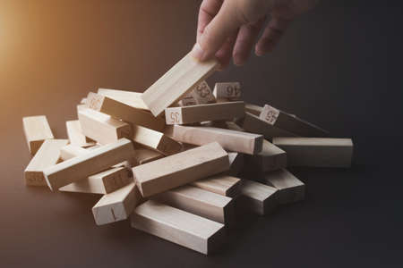 Hand pulls a wooden block from a pile of the same blocks on brown background with sunshine. Leader, individuality, best worker, best employee, idea, team. Business conceptual imageの写真素材