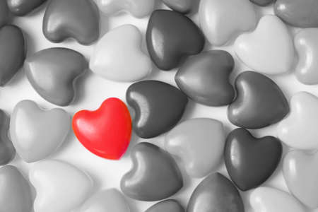 One red heart among a lot black and white hearts on white background top view. Background for...