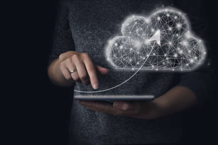 Hand touching tablet with arrow to low poly geometric cloud computing. The concept of working with...