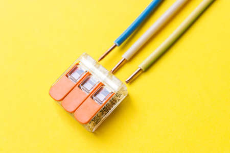 Compact splicing connector with wires phase, zero, ground on yellow background. Electronic...