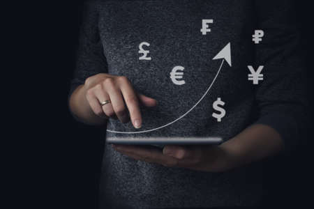 Hand holding tablet with a rising arrow and currency icons different countries. Business development to success and growing growth concept in 2021. Concept of money saving, financial. Successの写真素材