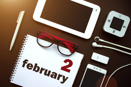 February 2nd. Day 2 of month, Calendar date. Office workplace with laptop, notebook, office supplies and stationery on brown back. Winter month, day of the year conceptの写真素材