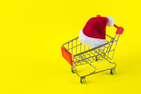 Red Santa's Christmas hat on yellow background in trolley cart on yellow backgroundの写真素材
