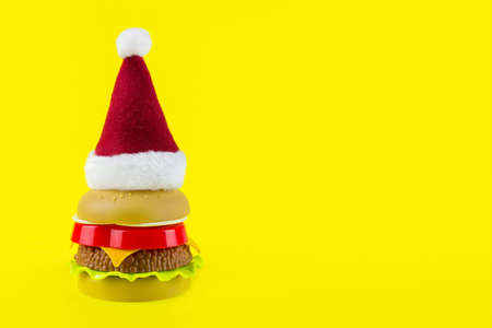 Toy burger with Santa's red hat on yellow background. Christmass fast foodの写真素材