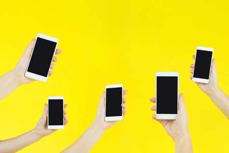 Cropped shot of hands holding smartphones on yellow.