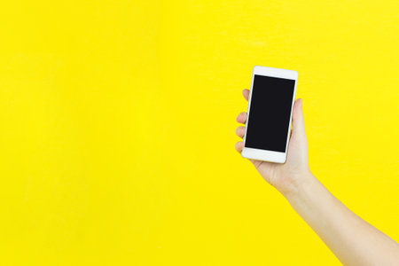 Smartphone in hand on yellow background with copy space for your text.の写真素材