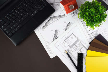 Architect workplace top view. White house on the construction drawings, laptop pen and color samplesの写真素材