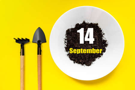 September 14th. Day 14 of month, Calendar date. White plate of soil with a small spatula and rake on yellow background. Autumn month, day of the year conceptの写真素材