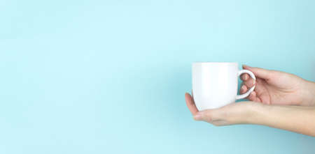 Close-Up Of Hands Holding Mug Over Blue Backgroundの写真素材