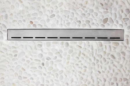Linear floor level shower. Metal drain on floor shower. Drainage on rocky floor at bathroomの写真素材