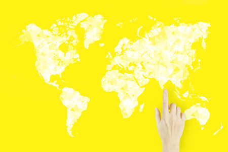 World map connection in hand. Global connection concept. Young woman's hand finger pointing with hologram on yellow backgroundの写真素材