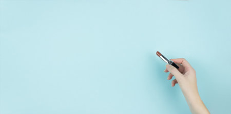 Cropped Hand Of Woman Holding Lipstick Against Blue Background.の写真素材