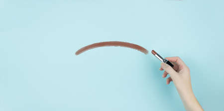 Hand of female writing negative smile with brown lipstick on blue background.の写真素材