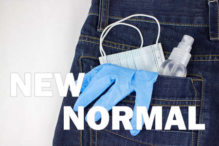 Blue medical mask, gloves and hand sanitizer spray looks out from back jeans pocket with inscription NEW NORMAL. Healthcare concept, Covid-19 concept.の写真素材