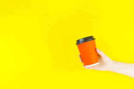 Hand holding coffee cup mockup blank on yellow background. Disposable coffee cup. Close-up, coffee to go.の写真素材
