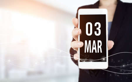 March 3rd. Day 3 of month, Calendar date. White smartphone with Calendar date in businesswoman hand on blurred background. Spring month, day of the year conceptの写真素材