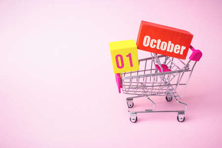 October 1st. Day 1 of month, Calendar date. Close up toy metal shopping cart with red and yellow box inside with Calendar date on pink background. Autumn month, day of the year conceptの写真素材