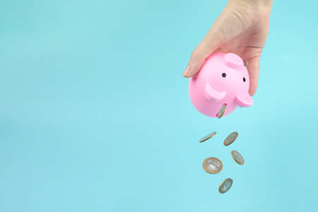 Close up hand shakes coins out of pink piggy bank, Falling Coins. Sale, buy, consumer saving, budget conceptの写真素材