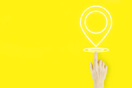 Pin address location concept. Young woman's hand finger pointing with hologram Location Marker on yellow background. Concept of Internet maps and navigationの写真素材