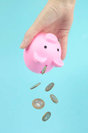 Hand shakes coins out of pink piggy bank, Falling Coins. The concept of saving money on shopping.の写真素材