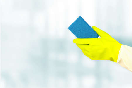 Spring cleaning concept. Top view of hands in rubber gloves holding sponge on blue background....
