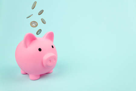 Pink piggy bank with Falling Coins on blue background. Financial savings and banking economyの写真素材