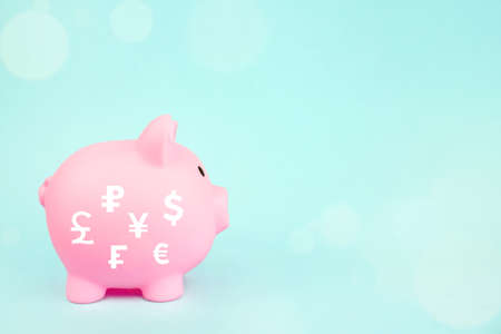 Pink piggy bank with digital hologram world currencies on blue background. Saving money wealth and financial concept.の写真素材