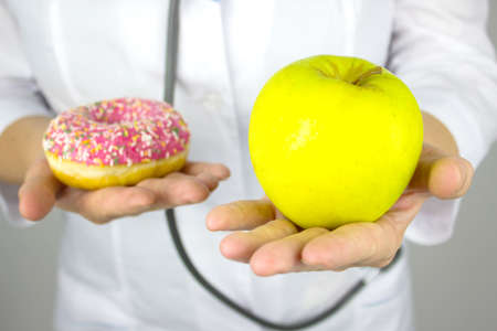 Medicine, healthcare concept. Close-up of the female doctor's hands with an apple and donut. Healthy diet. The concept of diet comparisonの写真素材