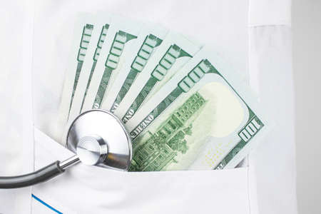 Paid medicine concept. Doctor's scrub pocket with stethoscope and US dollar bills