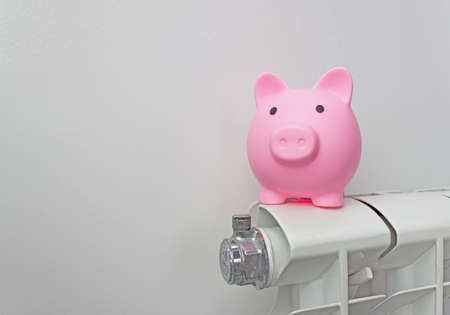 Piggy bank on radiator. Energy saving. Saving heating in winter. Expensive heating costs conceptの写真素材