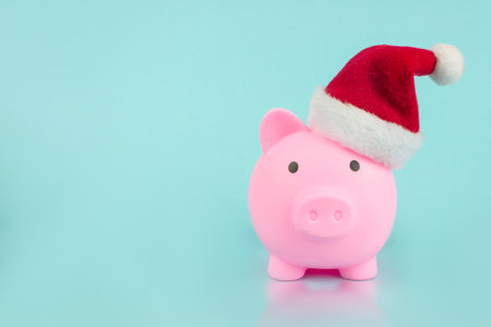 Christmas Piggy Bank. Christmas finances piggy bank wearing santa hat on blue background, copy space for text.の写真素材