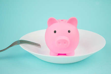 Plate with piggy bank with fork on blue background, savings consumer concept.の写真素材