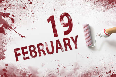 February 19th. Day 19 of month, Calendar date. The hand holds a roller with red paint and writes a calendar date on a white background. Winter month, day of the year conceptの写真素材