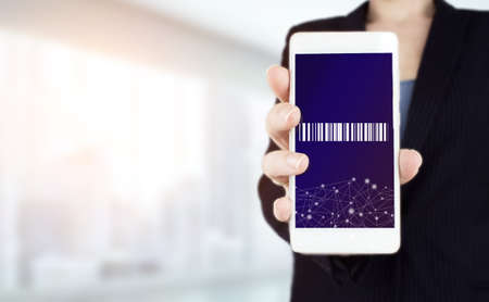 Inventory Logistics Concept. Hand hold white smartphone with digital hologram Bar Code Price Tag sign on light blurred backgroundの写真素材