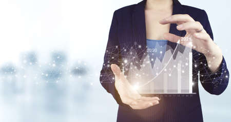 Concept for vision 2021-2022. Businessman welcome year 2022. Two hand holding virtual holographic growth graph chart icon with light blurred background. Business growth concept year 2022の写真素材