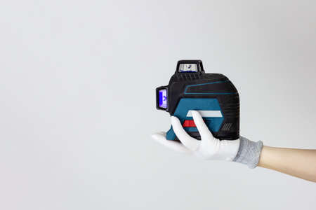 Gloved hands holding laser level construction tools. Work tools on white backgroundの写真素材